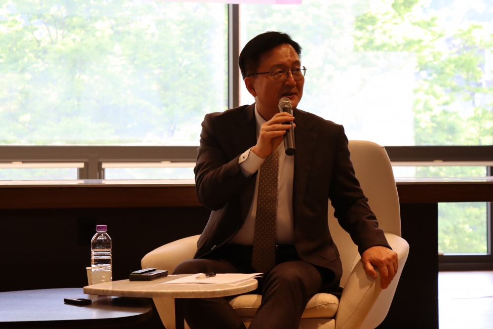 사진설명 시작. 의자에 앉아 있는 한 남성이 마이크를 들고 말하고 있다. 사진설명 끝.