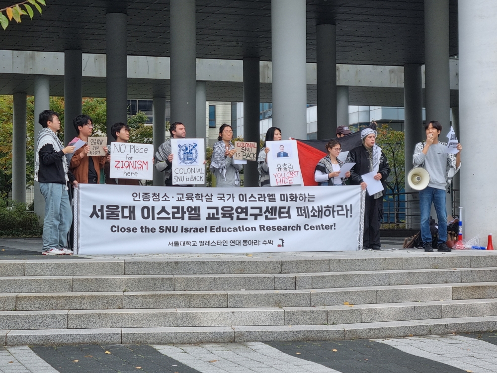 사진 설명 시작. 센터 입구에서 항의 행동이 진행되고 있다. 9명의 인물이 있고, 맨 오른쪽에 있는 인물은 스피커를 차고 발언하고 있다. 8명의 인물은 인종청소, 교육학살 국가 이스라엘 미화하는 서울대 이스라엘 교육연구센터 폐쇄하라! 라고 쓰인 큰 플랜카드를 뒤에서 colonial snu is back 등의 문구가 쓰인 피켓을 들고 시위에 참여하고 있다. 사진 설명 끝.