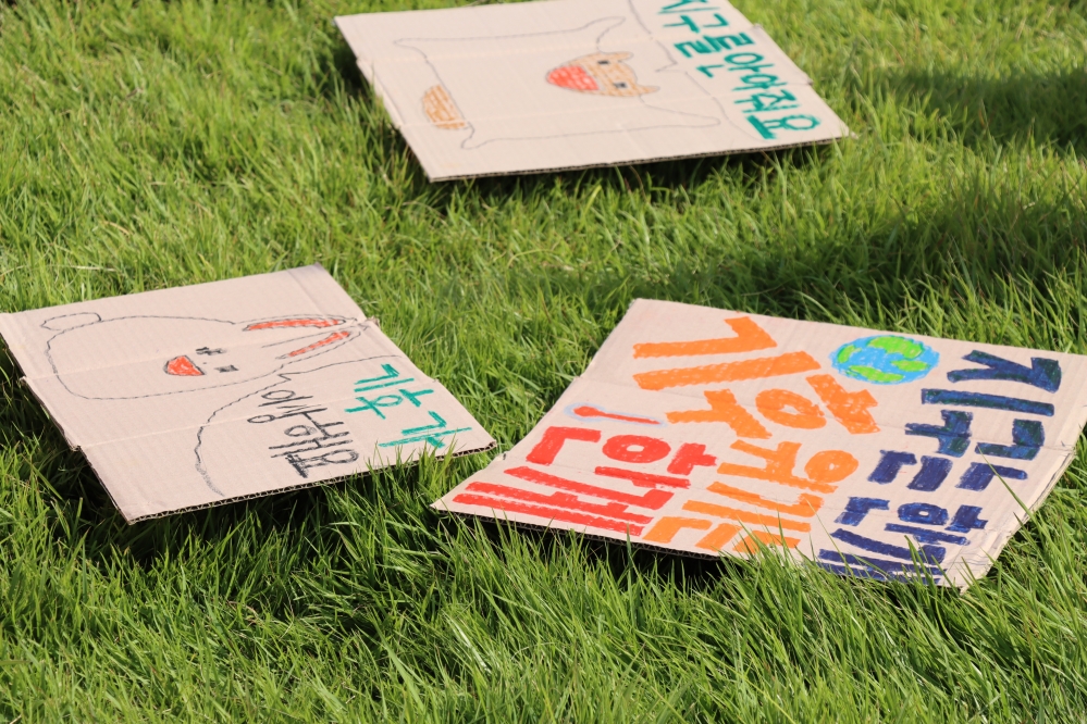 사진 설명 시작. 퍼포먼스 중, 학생들이 들고 있던 피켓 외에도 땅바닥에는 몇 개의 피켓이 떨어져있었다. 문구는 위에서부터 차례로 '지구를 안아줘요', '기후가 이상해요', '지구는 한 개, 기후위기는 한계'라고 적혀있다. 기사 설명 끝.