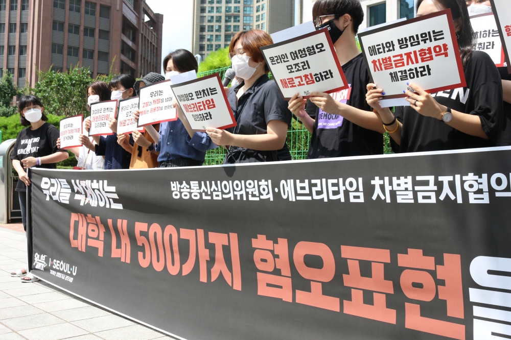 대체로 검은 옷을 입은 기자회견 참여자들이 가로로 긴 현수막을 뒤에 나란히 일렬로 서있다.