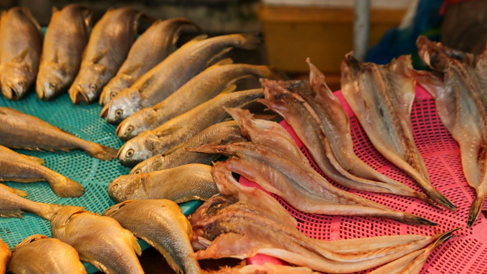 사진 설명 시작. 소쿠리 두 개 위에는 생선들이 가득하다. 왼쪽 초록색 소쿠리에는 손질되지 않은 원형의 생선들이 있다. 반면 오른쪽 빨간색 소쿠리에는 반으로 갈라진 채 건조된 생선들이 자리한다. 사진 설명 끝.