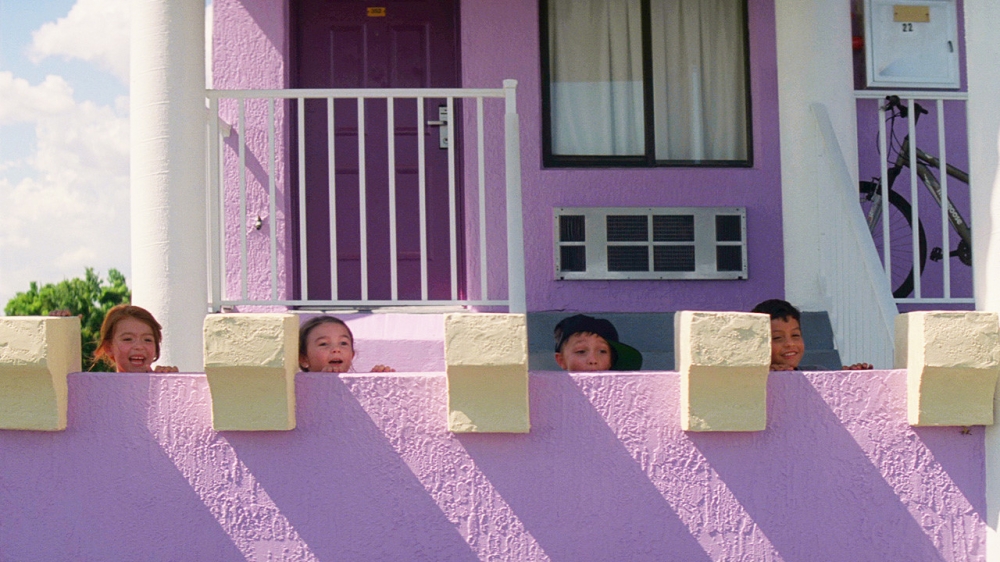 보라색으로 칠해진 모텔인 매직 캐슬의 난간에 무니와 친구들이 기대어 있다. 지나가는 사람에게 침을 뱉으면서 놀려고 기다리고 있다. 사진 설명 끝.