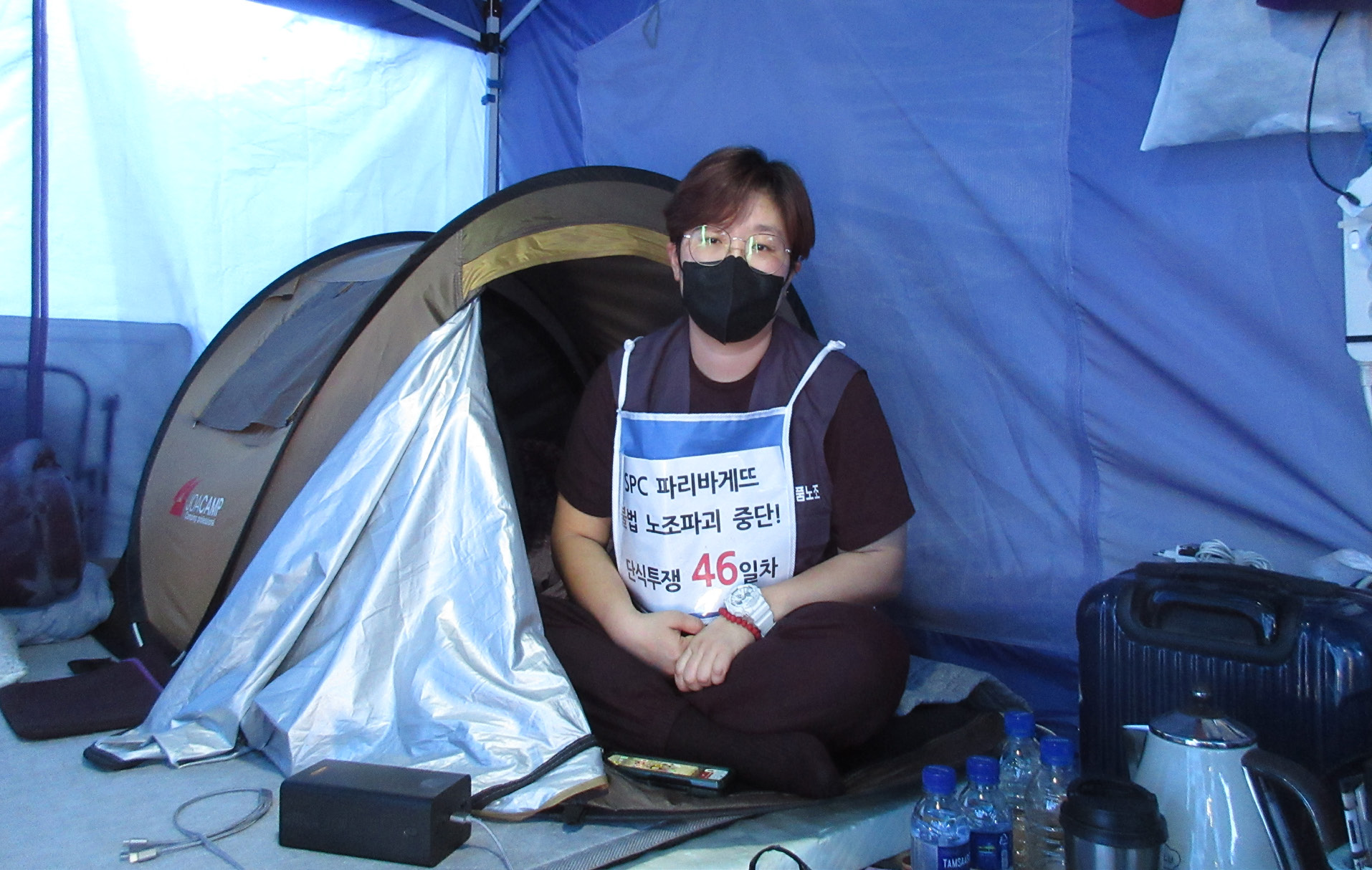 사진 설명 시작. 임종린 지회장이 SPC 본사 앞 천막에 앉아 단식 농성을 벌이고 있다. 착용하고 있는 조끼 위에는 SPC 파리바게뜨 불법 노조파괴 중단! 단식투쟁 46일차라고 적혀 있다. 사진 설명 끝.