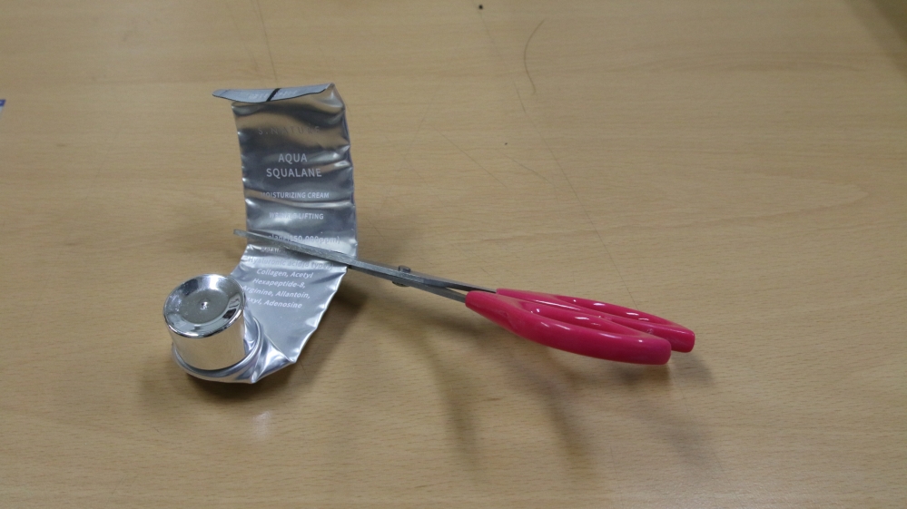 사진 설명 시작. 수분 크림 튜브를 가위로 자르고 있다. 사진 설명 끝.