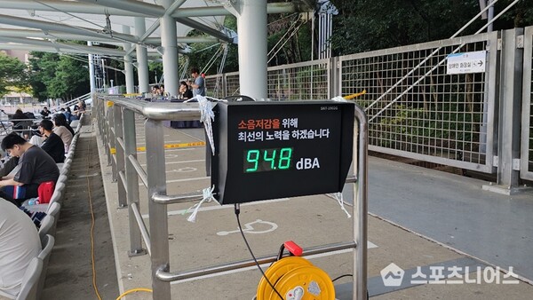사진설명 시작. 왼쪽에 관중이 몇몇 앉아있다. 가운데에는 ‘소음저감을 위해 최선의 노력을 하겠습니다’가 적혀 있고, 그 아래 ’94.8 dBA’가 표시돼 있는 전광판이 있다. 사진설명 끝.