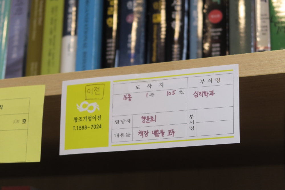 책장에 이사를 위한 분류표가 붙어 있다. 이 책장을 16동 1층 105호로 이전해야 한다는 내용이 적혀 있다. 사진 설명 끝.