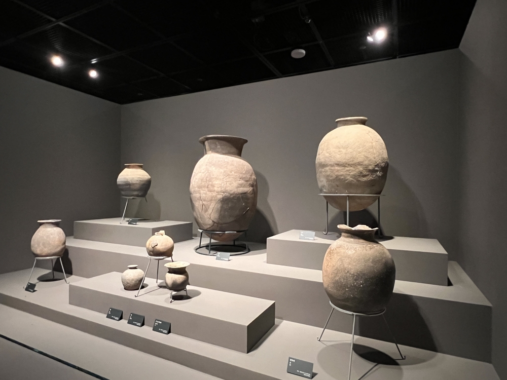사진 설명 시작. 몽촌토성 저장구덩이에서 출토된 항아리 8점이 전시되어 있다. 전시 공간은 유리 없이 열린 공간으로 계단형의 단 위에 각각 항아리가 놓여있다. 가운데에 가장 큰 크기의 항아리가 있고 오른쪽에 그와 유사한 크기의 항아리가 한 단 위에 있다. 그 아래로 중간 크기의 둥근 항아리가 있다. 가운데 아랫단에 작은 항아리 세 점이 전시되어 있고 왼쪽으로는 서로 다른 단에 각각 하나씩 두 항아리가 진열돼있다. 사진 설명 끝.
