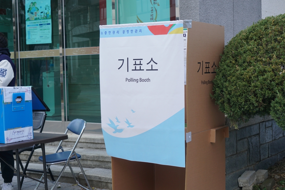사진 설명 시작. 야외에 총학생회 선거를 위한 기표소가 설치되어 있다. 기표소 입구에