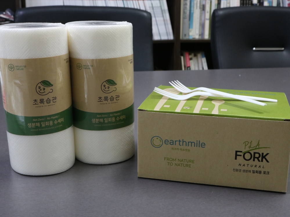 사진 설명 시작. 흰색 원기둥 모양의 생분해 일회용 수세미 두 개가 포장되어 좌측에 놓여있다. 우측에는