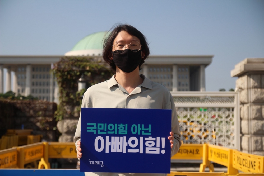 사진 설명 시작. 이성윤 대표가 국회의사당 앞에서 플랜카드를 들고 서 있다. 플랜카드에는