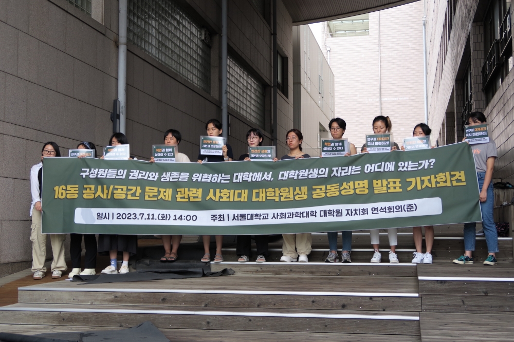 사진 설명 시작. 16동 앞 계단에서 대학원생들이 현수막과 피켓을 들고 서 있다. 현수막에는