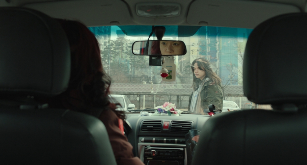 사진 설명 시작. 수경이 운전석에 앉아 바깥의 이정을 바라보고 있다. 수경의 얼굴이 백미러를 통해 보인다. 이정은 바깥인 주차장에 서서 차 안의 수경을 노려보고 있다. 사진 설명 끝.