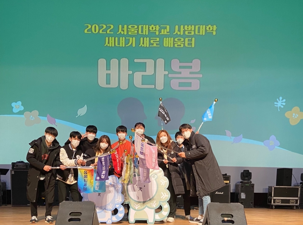 사진 설명 시작. 푸른 배경을 바탕으로 2022 서울대학교 사범대학 새내기 새로 배움터 바라봄이라고 써진 배경 앞에 여러 학생들이 각 과반의 명칭이 쓰인 깃발을 들고 있다. 사진 설명 끝.