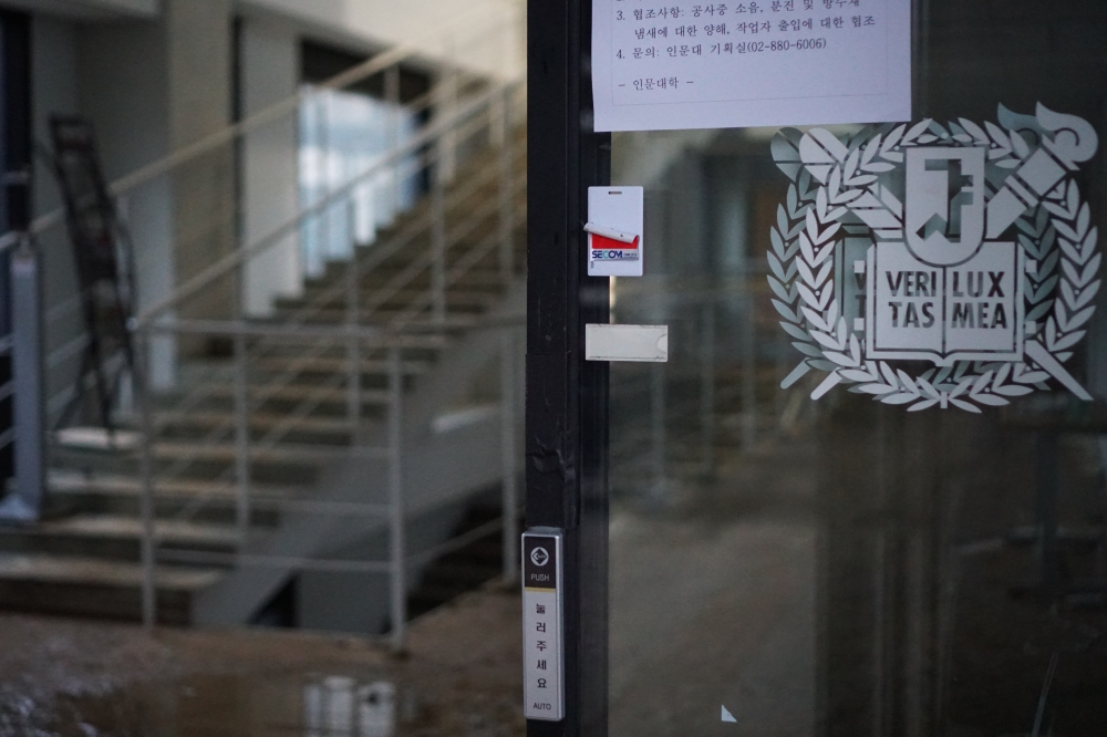 사진 설명 시작. 인문대 건물의 서울대학교 로고가 그려진 유리문 뒤에 흙탕물로 뒤덮인 계단이 있다. 사진 설명 끝.