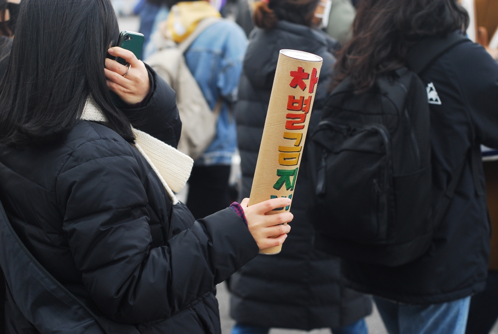 사진 설명 시작. 행진에 참여한 시민의 손에는 차별금지법이라는 문구가 무지개 색으로 적힌 소품이 들려 있다. 사진 설명 끝.