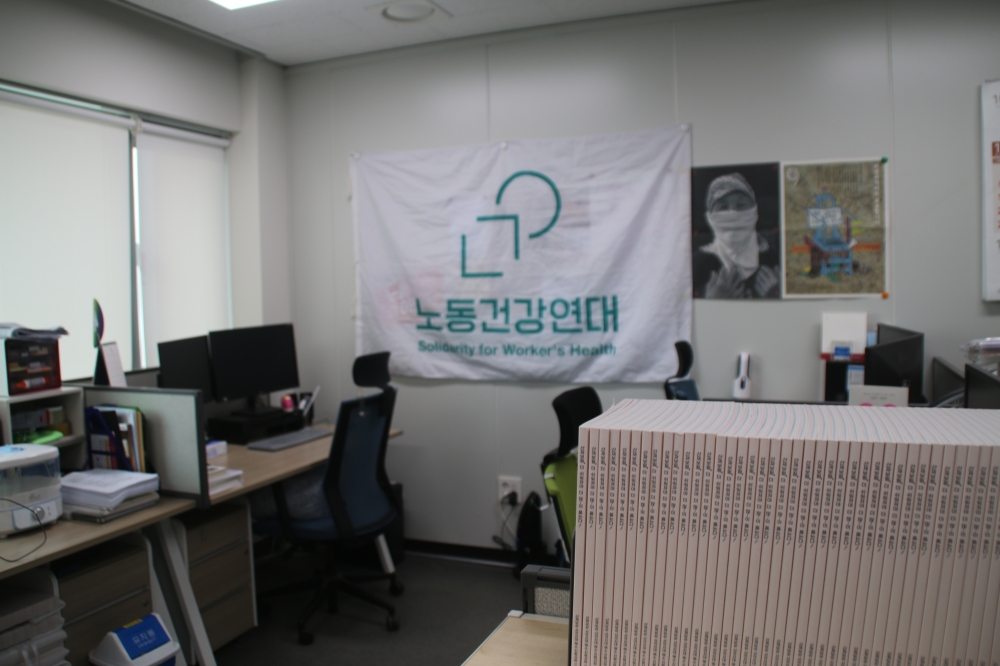사진 설명 시작. 노동건강연대 사무실 내부. 사무용 책상과 자료집, 벽면에는 노동건강연대 깃발과 각종 포스터들이 있다. 사진 설명 끝.