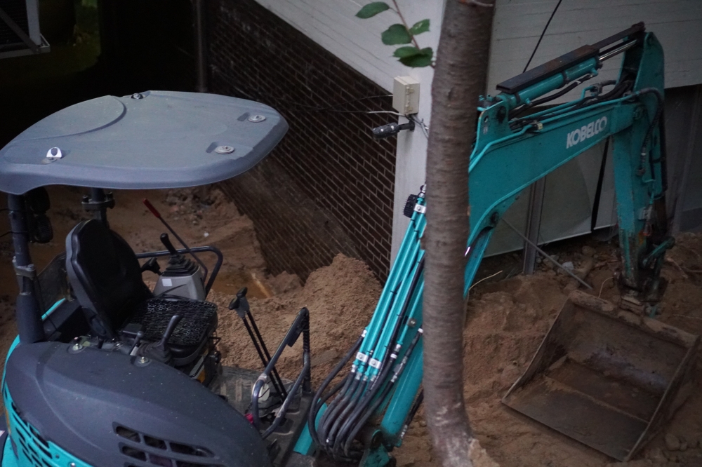 사진 설명 시작. 흙 사이에 청록색 포크레인이 주차돼 있다. 포크레인 앞에는 나뭇가지가 있다. 사진 설명 끝.