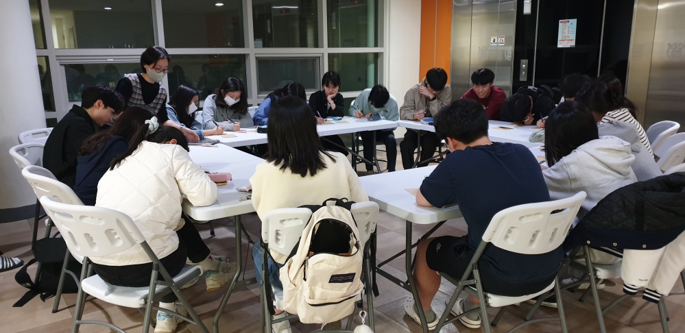 사진 설명 시작. 직사각형 모양으로 배치된 테이블에 학생들이 모여앉아 필기를 해가며 주제에 대한 대화를 나누고 있다. 사진 설명 끝.