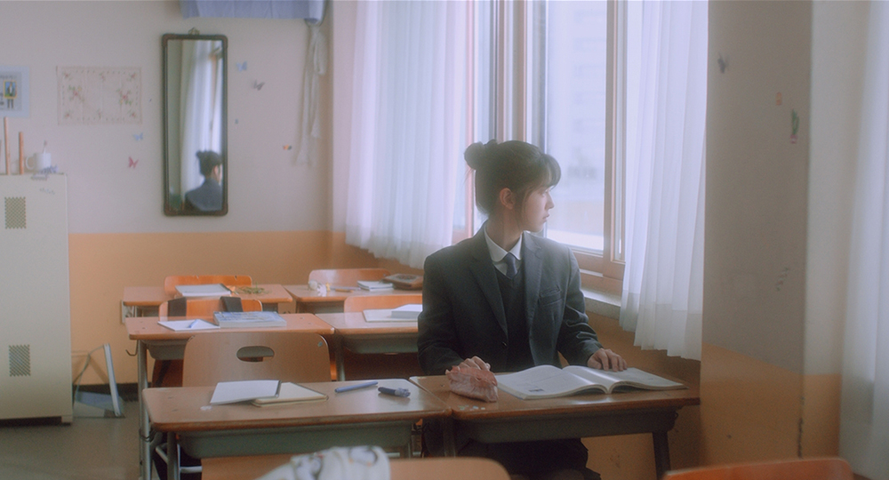 사진 설명 시작. 고등학교 교실이다. 세미가 자리에 앉아 창밖을 바라보고 있다. 사진 설명 끝.