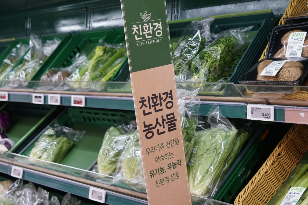 사진 설명 시작. 대형마트 냉장 가판대의 초록색 크레이터에 비닐에 싸인 배추, 시금치 등 각종 채소가 진열돼 있다. 가판대에는 초록색 배너가 걸려 있다. 배너에는 친환경 농산물이라는 글씨가 쓰여 있다. 사진 설명 끝.