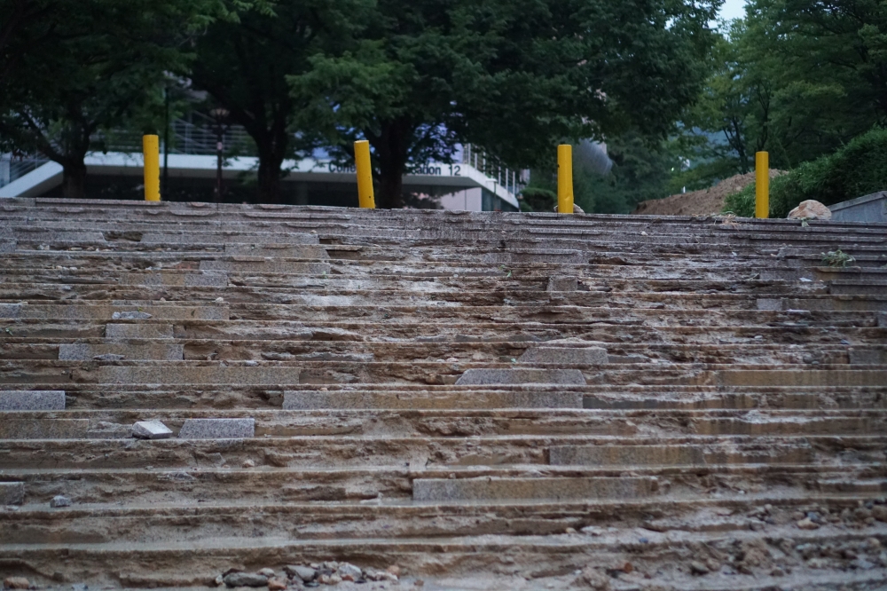 사진 설명 시작. 계단을 아래에서 찍었고, 계단이 망가져 있고, 계단 위쪽에는 네 개의 노란색 기둥이 있다. 사진 설명 끝.