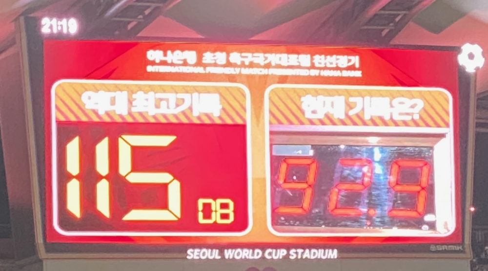 사진설명 시작. 전광판을 찍은 사진이다. 왼쪽 위에 ’21:19’로 시간이 표시돼 있다. ‘하나은행 초청 축구국가대표팀 친선경기’가 전광판 중앙 맨 위에 써있고, 그 아래 ‘역대 최고기록’과 ‘현재 기록은?’이 적혀 있어 소음 크기를 비교하고 있다. 역대 최고기록은 ‘115 DB(데시벨)’로 써있고, 현재 기록은 ’92.9’로 써있다. 아래는 ‘SEOUL WORLD CUP STADIUM’이 새겨진 전광판이다. 사진설명 끝.