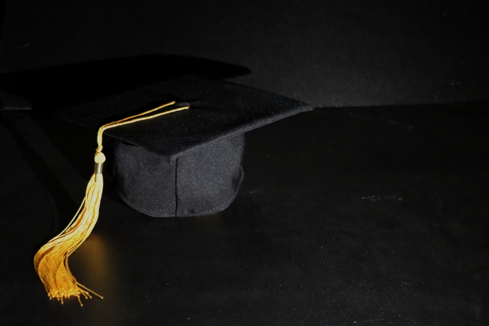 사진 설명 시작. 검은색 배경에 학사모가 놓여 있다. 학사모 위로는 노란색 수술이 늘어져 있다. 사진 설명 끝.