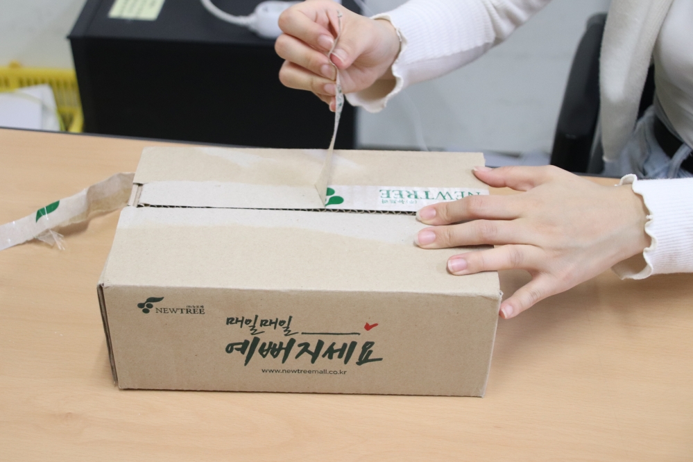 사진 설명 시작. 택배 상자 위에 붙은 테이프를 떼어 내고 있다. 사진 설명 끝.