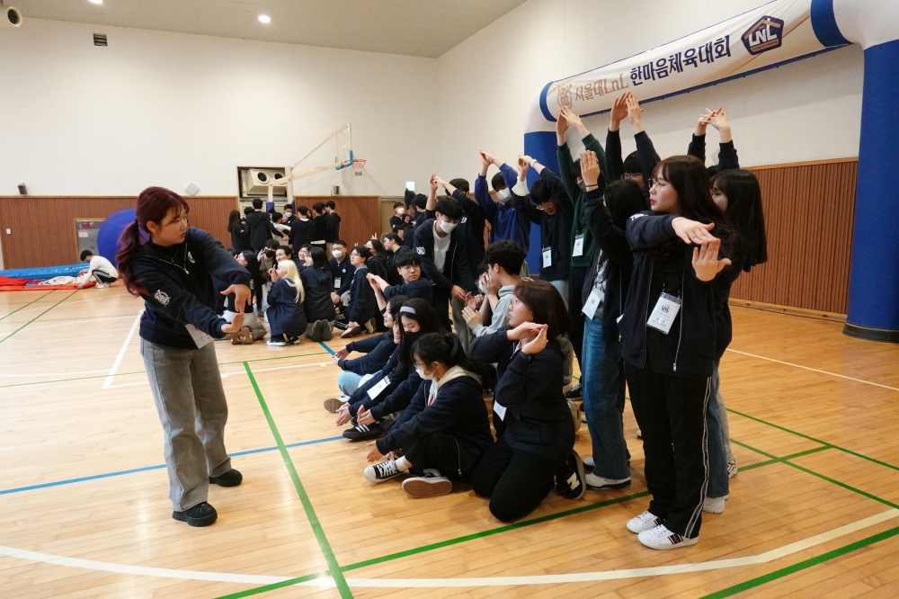 사진 설명 시작. 체육관에 체육복을 입은채 모인 학생들이 조교의 시범에 따라 스트레칭을 하고 있다. 사진 설명 끝.