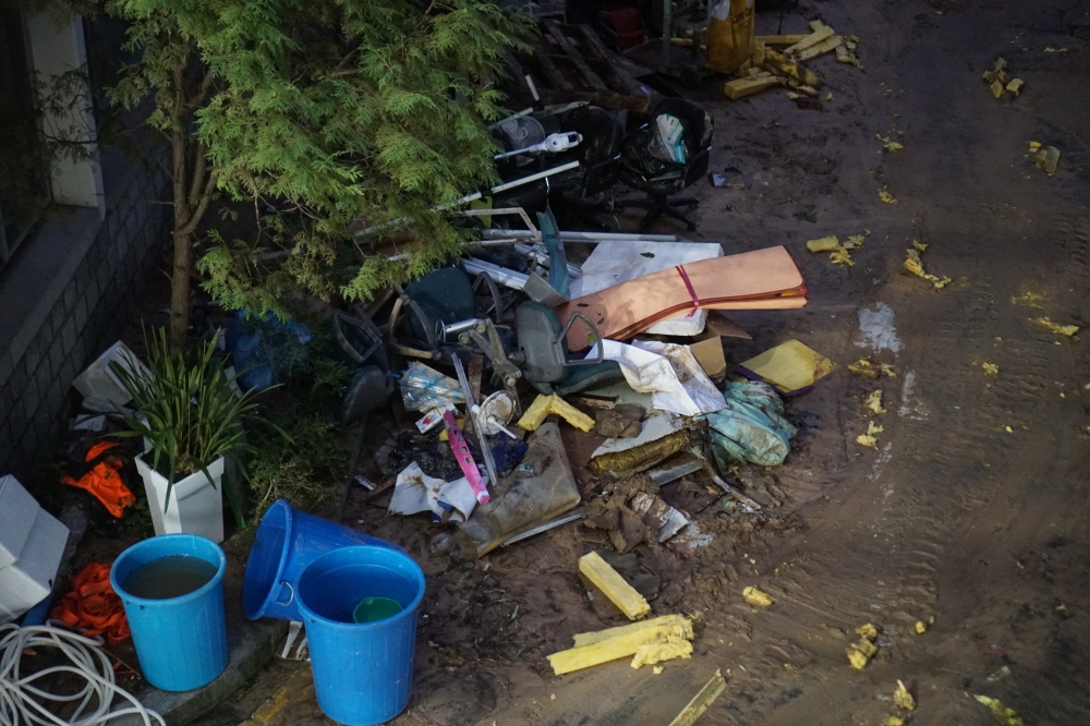 사진 설명 시작. 나무 아래 흙바닥에 세계의 파란색 통과 노란색 스티로폼 쓰레기, 주황색 종이 쓰레기를 비롯한 여러 쓰레기들이 나뒹굴고 있다. 사진 설명 끝.