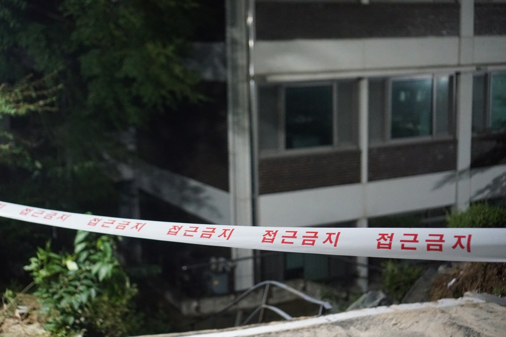 사진 설명 시작. 빨간 글씨로 접근금지라고 적힌 하얀 띠가 있고 그 뒤에는 인문대학교 건물과 휜 계단 손잡이가 있다. 사진 설명 끝.