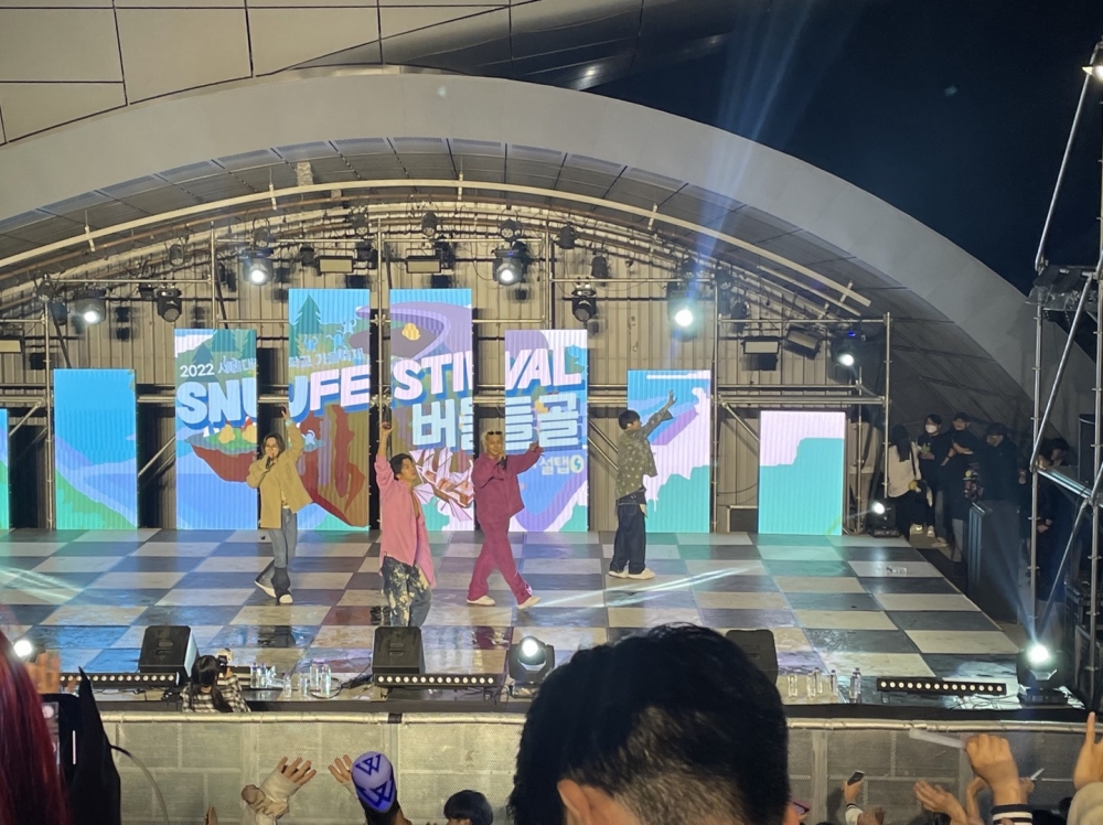 사진 설명 시작. 버들골 무대 위에 초대 가수 위너 멤버 4명이 공연 중이다. 마이크를 들고 손을 서 있다. 뒤에는 SNU FESTIVAL 버들골이라 적힌 화면을 송출 중인 판넬들이 있다. 관객들이 손을 들고 공연에 호응하고 있다. 사진 설명 끝.