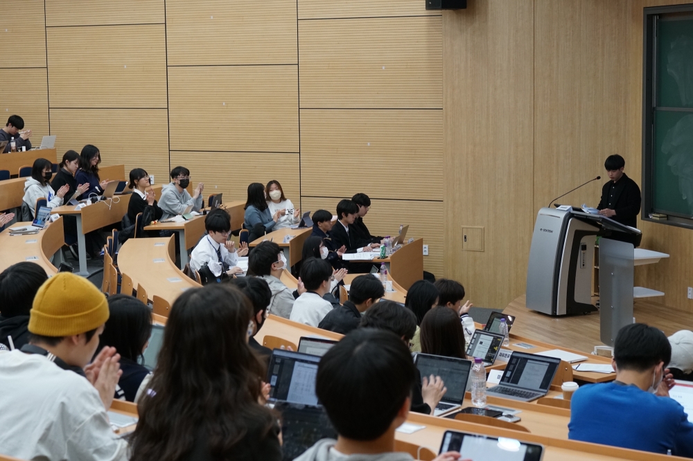 사진 설명 시작. 계단식 강의실에 대의원들이 앉아 있다. 연단에 선 조재현 총학생회장이 발언하고 있다. 사진 설명 끝.