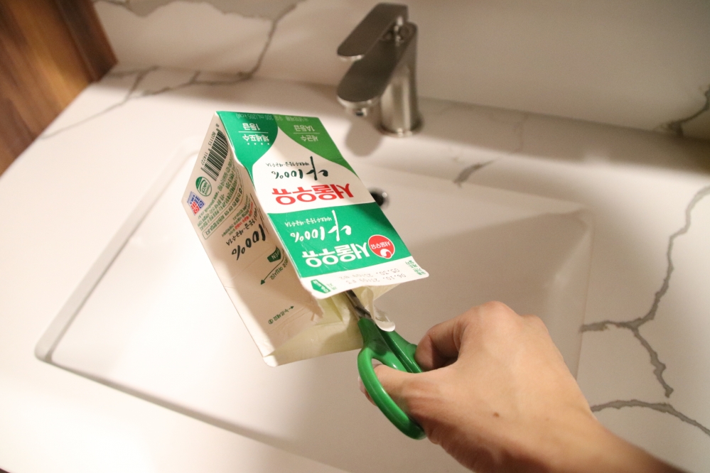 사진 설명 시작. 우유팩을 가위로 자르고 있다. 사진 설명 끝.