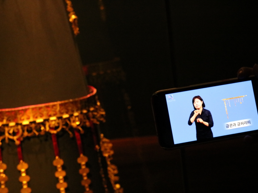 사진 설명 시작. 사진 왼쪽에는 신라 시대의 금허리띠가 전시돼 있다. 오른쪽에는 금허리띠에 대한 수어해설 영상을 띄워놓은 기자의 휴대폰 화면이 있다. 사진 설명 끝.