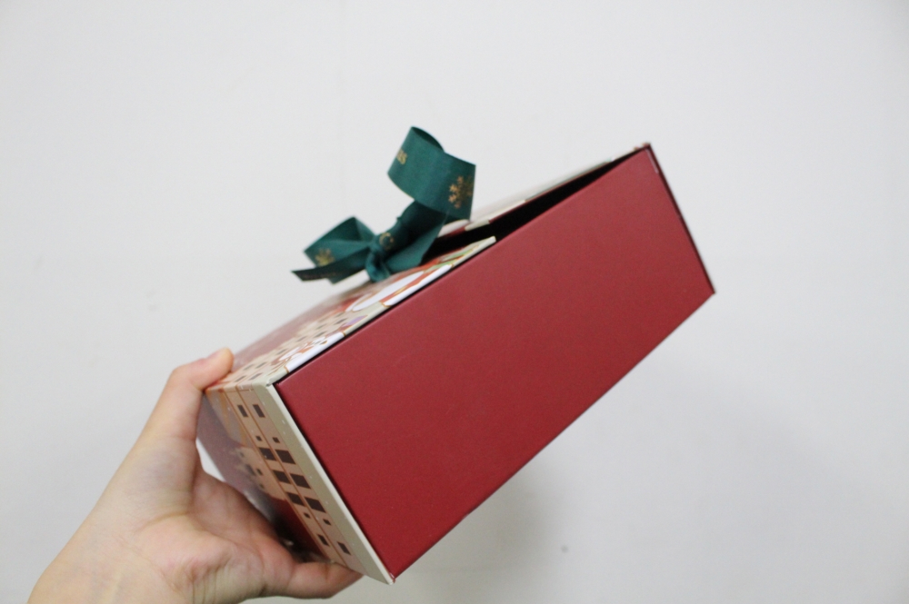 사진 설명 시작. 빨간색 상자에 초록색 리본으로 장식된 선물상자를 들고 있다. 사진 설명 끝.