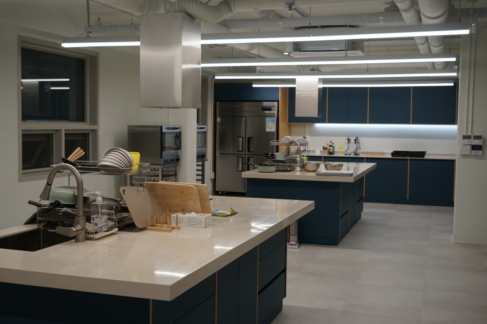 사진 설명 시작. 흰색과 탁한 하늘색이 섞인 가구와 흰색 페인트가 칠해진 주방이다. 도마, 접시 등의 주방용품이 싱크대 옆에 가지런히 정리되어 있다. 사진 설명 끝.