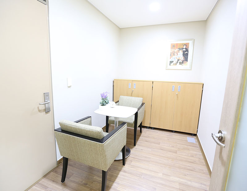 사진 설명 시작. 하얀 방 안의 모습이다. 의자 두 개 사이에 테이블이 하나 놓여 있다. 뒤쪽에는 서랍이 보인다. 사진 설명 끝.