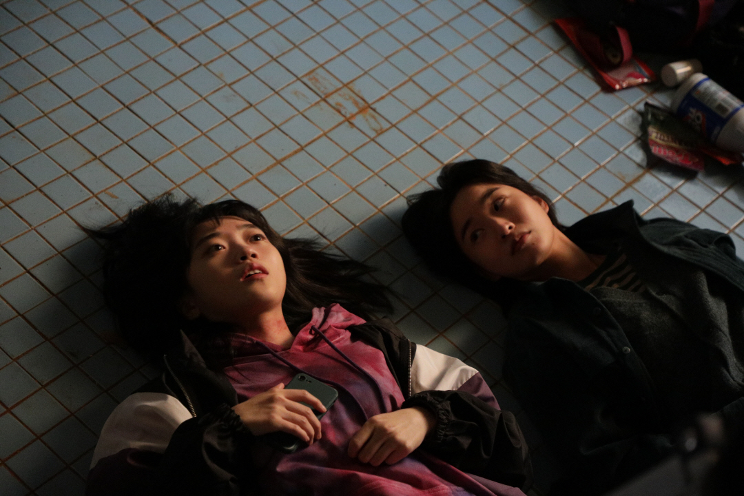 사진 설명 시작. 하늘색 타일이 깔린 바닥에 선우와 나미가 누워 있다. 나미는 천장을 바라보며 무언가 말하고 있고, 선우는 나미를 바라보고 있다. 사진 설명 끝.