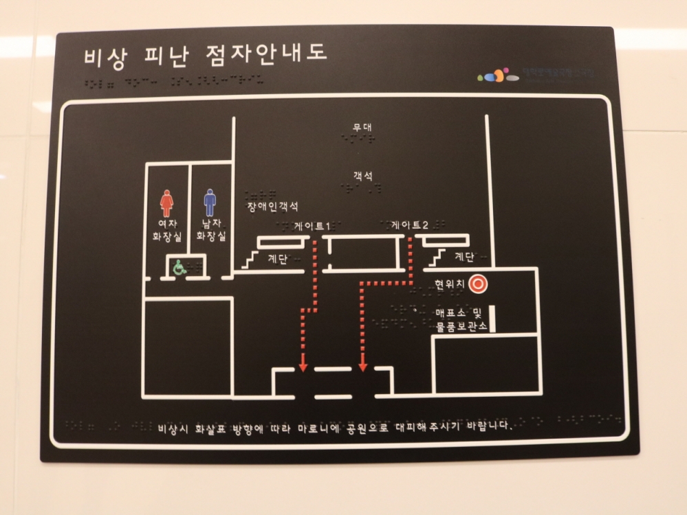 져 있으며, 비상 상황 발생시 도우미들이 맬 수 있는 끈이 양쪽에 달려 있다. 사진 설명 끝. 사진 설명 시작. 대학로예술극장 지하의 점자 비상대피 안내도이다. 사진 설명 끝.