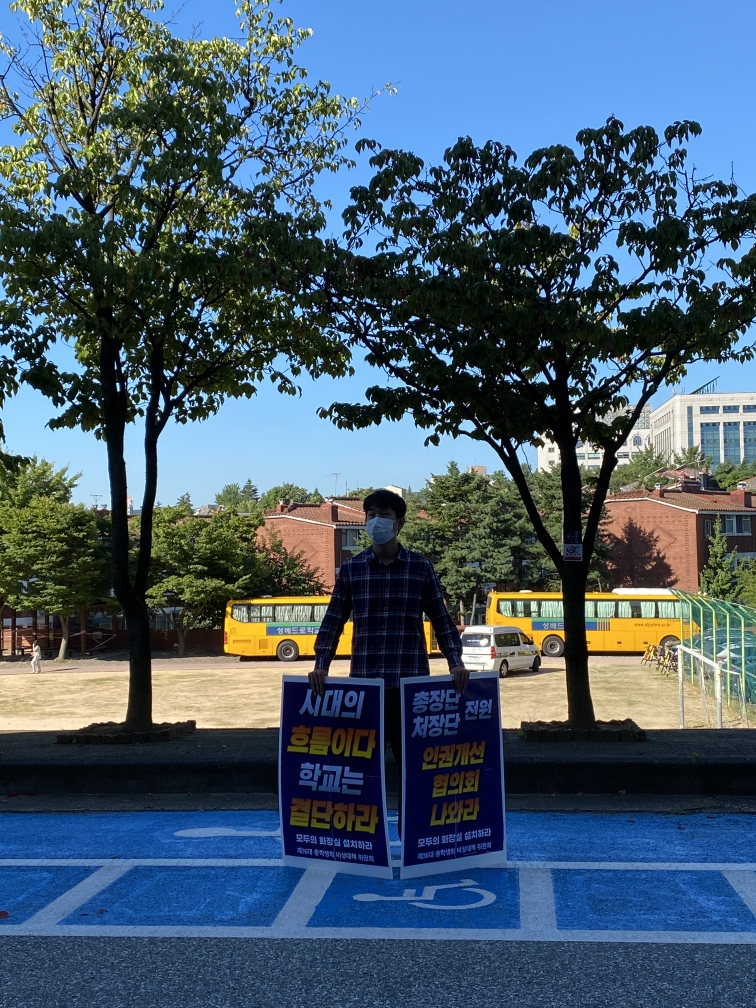 사진 설명 시작. 이훈 비대위장이 성공회대 장애인 주차장에서 플랜카드를 들고 서 있다. 플랜카드에는