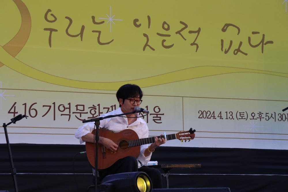 사진 설명 시작. 루시드폴이 무대 위 의자에 앉아 기타를 들고 노래를 부르고 있다. 사진 설명 끝.