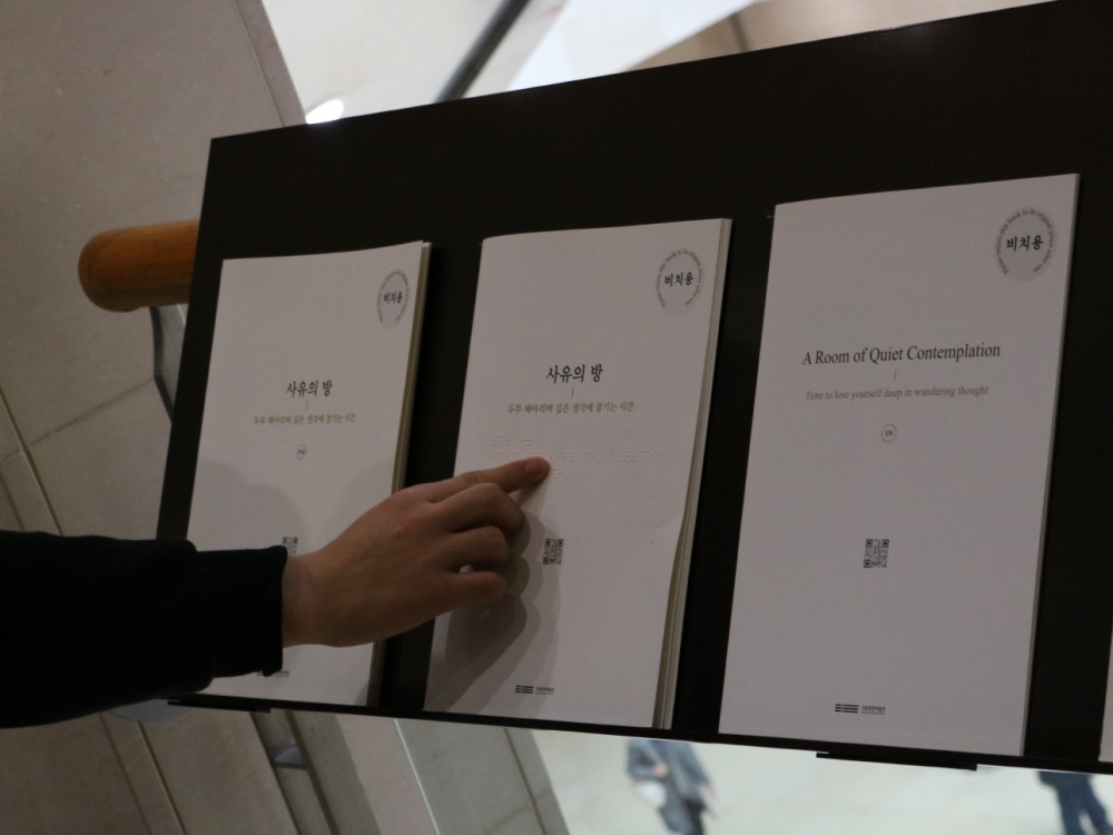 사진 설명 시작. 사유의 방 앞에 한국어, 점자, 영어로 된 팸플릿이 나란히 놓여 있다. 기자의 손이 점자 팸플릿을 짚고 있다. 사진 설명 끝.