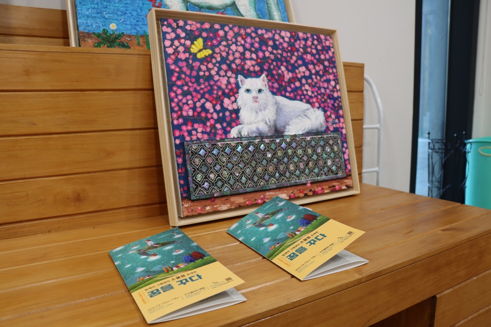 사진 설명 시작. 흰 고양이가 자개 장식 위에 앉아 있다. 이정옥 작가 작품. 사진 설명 끝.