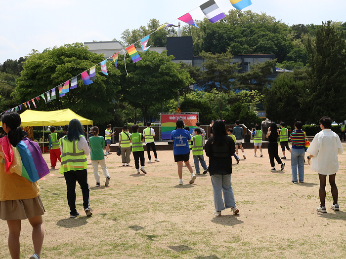 사진 설명 시작. 오색의 깃발 아래 행사 참가자들이 서로간 대형을 이뤄 손목돌리기를 하며 몸풀기 체조를 하고 있다. 정면 무대에