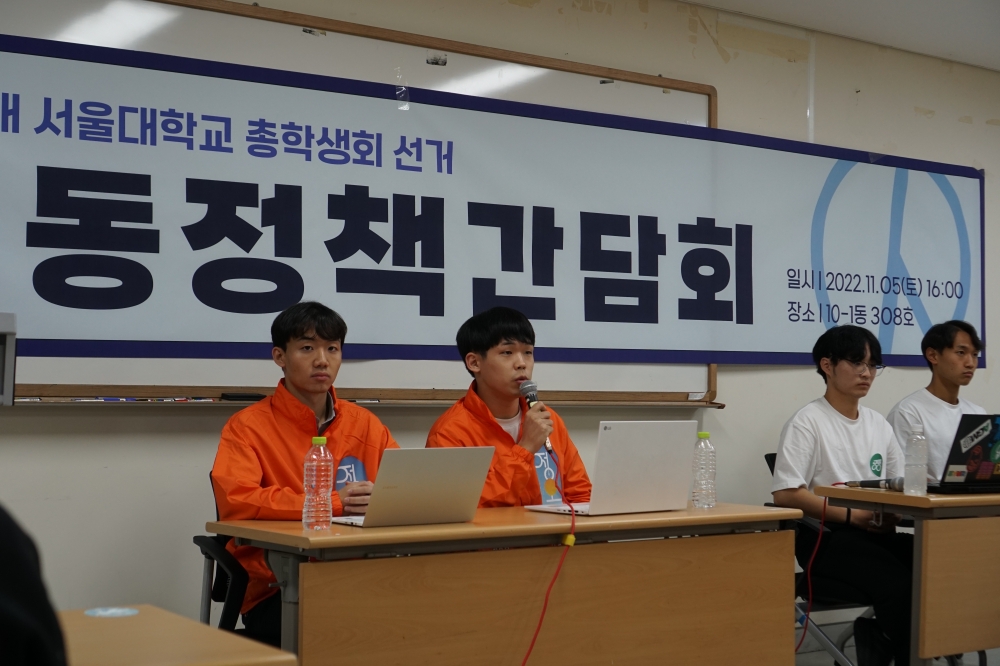 사진 설명 시작. 강의실 앞쪽에 두 개의 책상이 놓여 있다. 두 책상에 각각