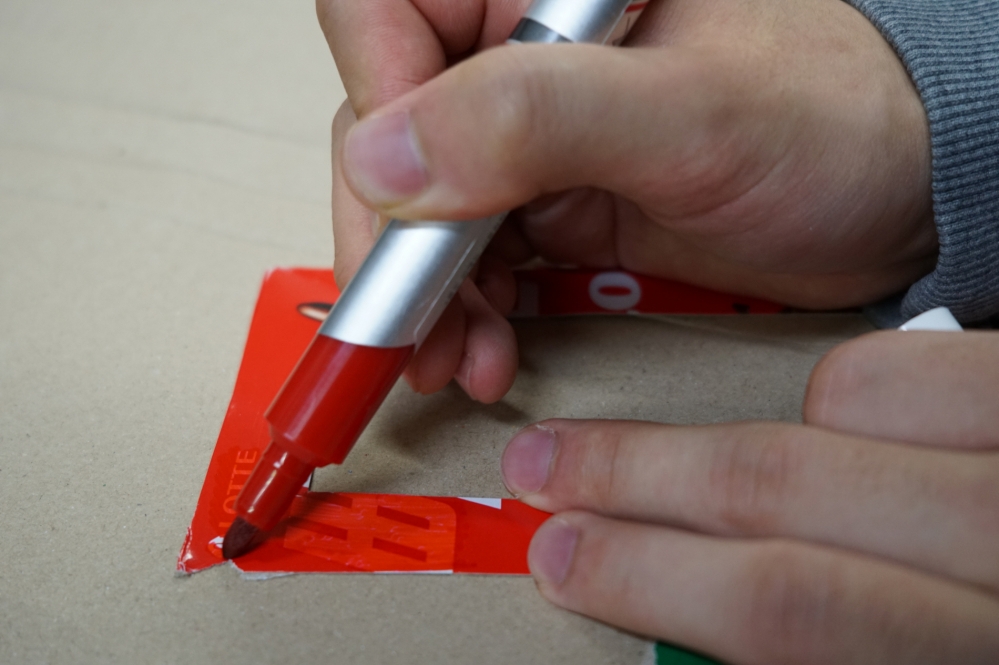 사진 설명 시작. 잘라낸 과자 상자를 매직으로 칠하고 있다. 사진 설명 끝.