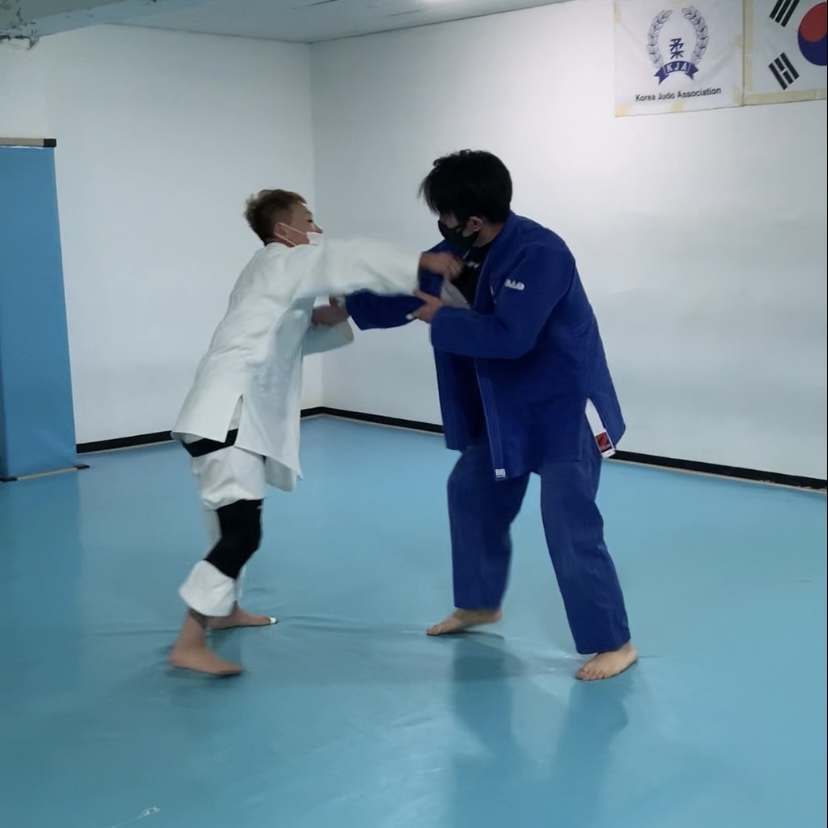 사진 설명 시작. 성현 씨가 유도장에서 흰 유도복을 입고 파란 유도복을 입은 상대와 대련하고 있다. 상대의 가슴팍을 붙잡으려 하고 있다. 사진 설명 끝