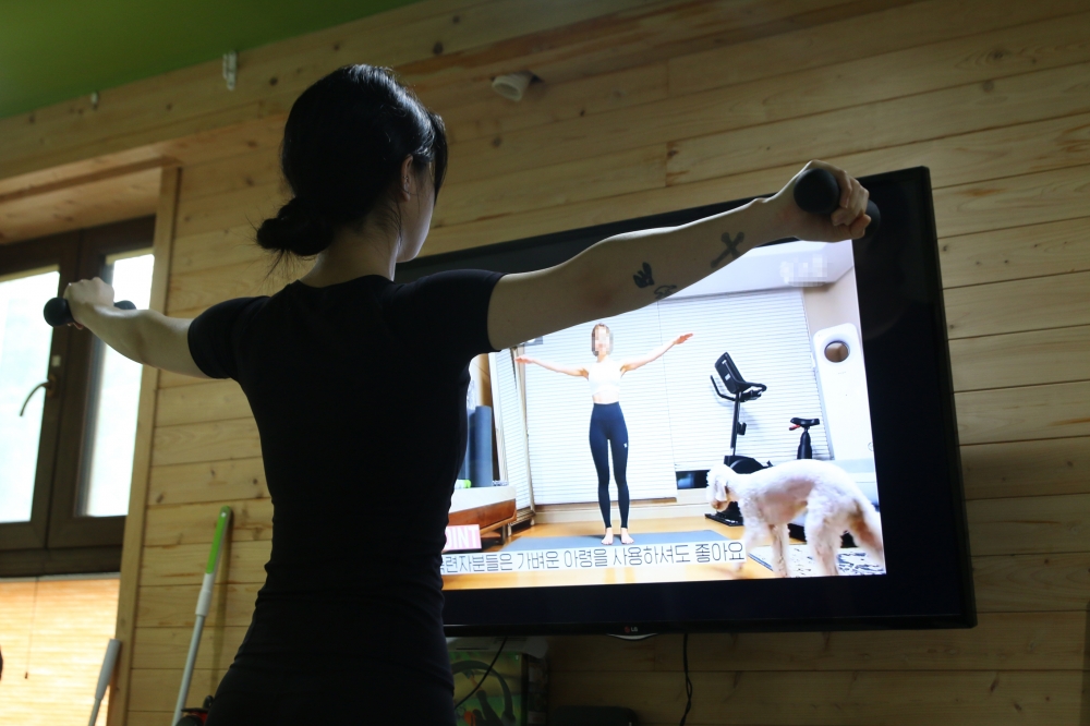 사진설명 시작. 운동복을 입은 혜진 씨가 유튜브로 홈트레이닝 영상을 틀어 놓고 따라하고 있다. 아령을 들고 팔 동작을 하고 있다. 사진 설명 끝