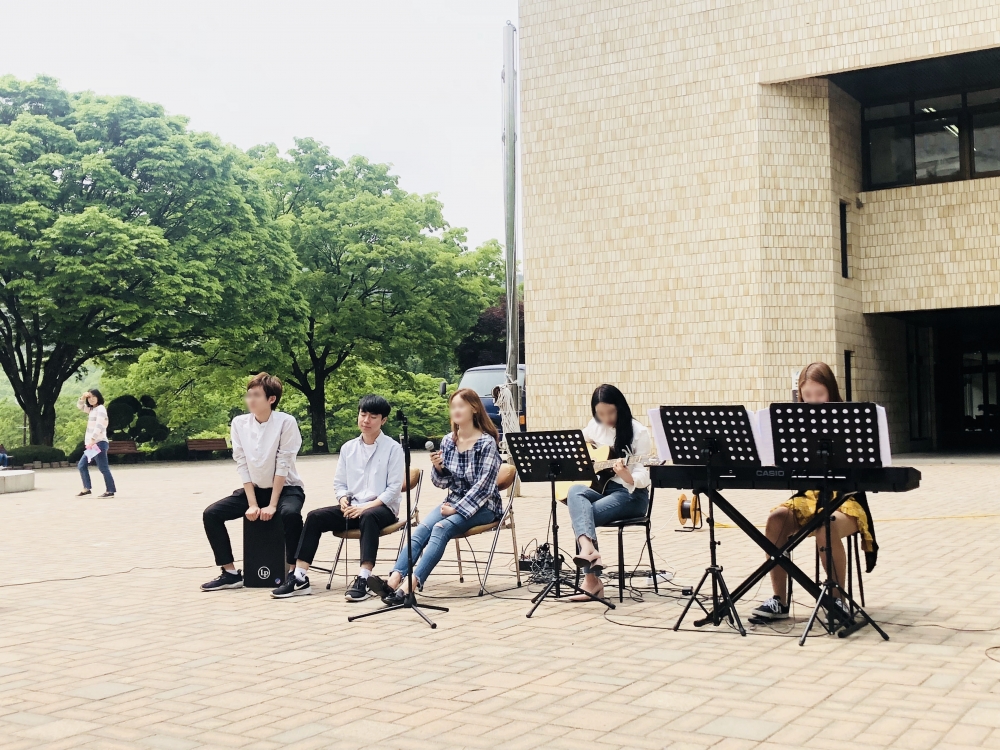 사진 설명 시작. 문화관 앞에 다섯 명의 사람이 나란히 앉아 악기를 연주하고 있다. ▲최강우 씨가 활동했던 밴드의 문화관 공연 모습이다. 사진 설명 끝.